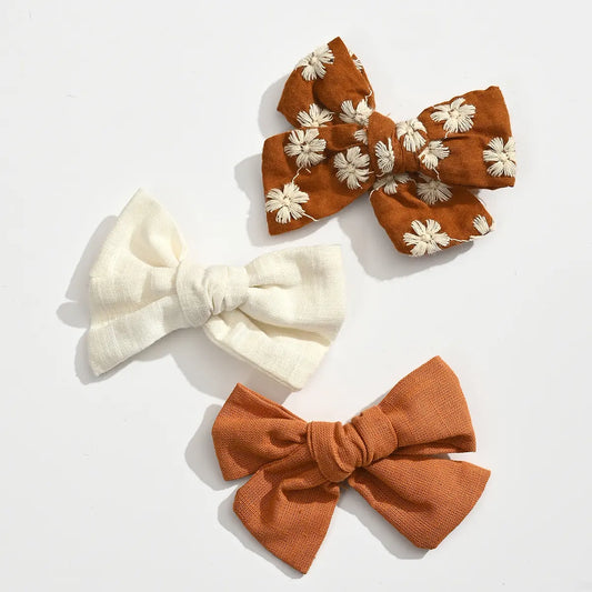Lot de 3 barrettes pince croco fille avec nœuds en tissu aux tons doux. Accessoires cheveux élégants et confortables pour bébé et enfant.