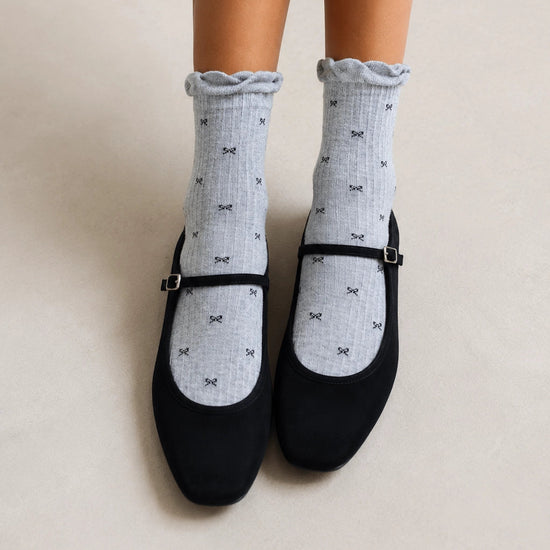 Chaussettes montantes tige côtelée. Motif petit noeud noir. Finition volant sur le haut de tige. Disponibles en blanc, gris chiné clair et noir. 