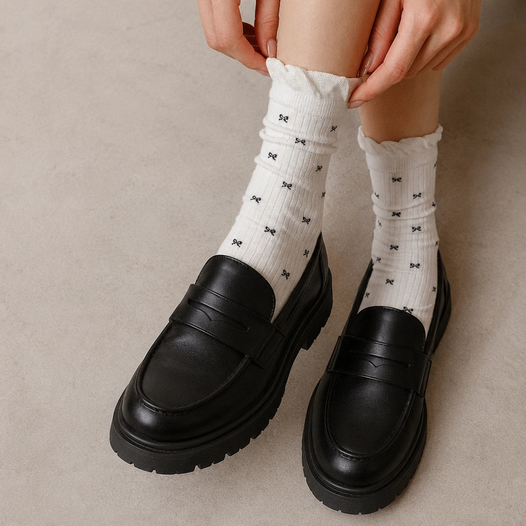 Chaussettes montantes tige côtelée. Motif petit noeud noir. Finition volant sur le haut de tige. Disponibles en blanc, gris chiné clair et noir. 