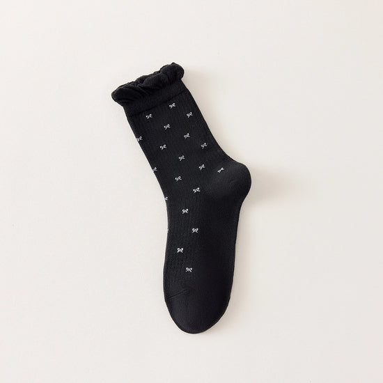 Chaussettes montantes tige côtelée. Motif petit noeud noir. Finition volant sur le haut de tige. Disponibles en blanc, gris chiné clair et noir. 