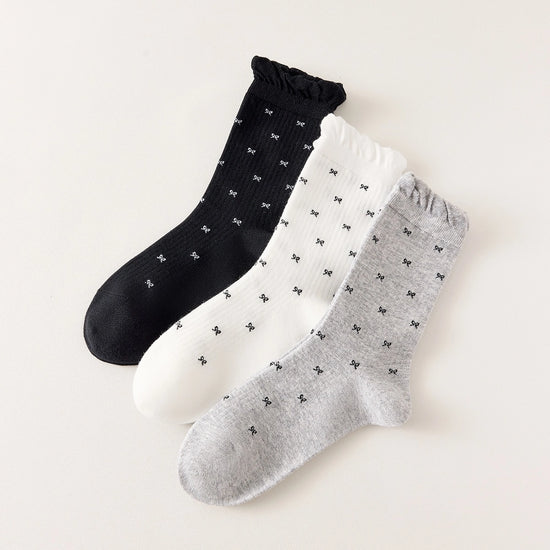 Chaussettes montantes tige côtelée. Motif petit noeud noir. Finition volant sur le haut de tige. Disponibles en blanc, gris chiné clair et noir. 