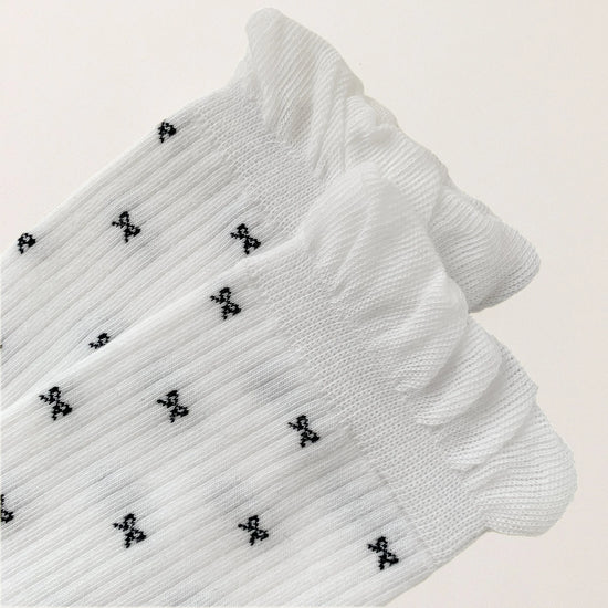 Chaussettes montantes tige côtelée. Motif petit noeud noir. Finition volant sur le haut de tige. Disponibles en blanc, gris chiné clair et noir. 