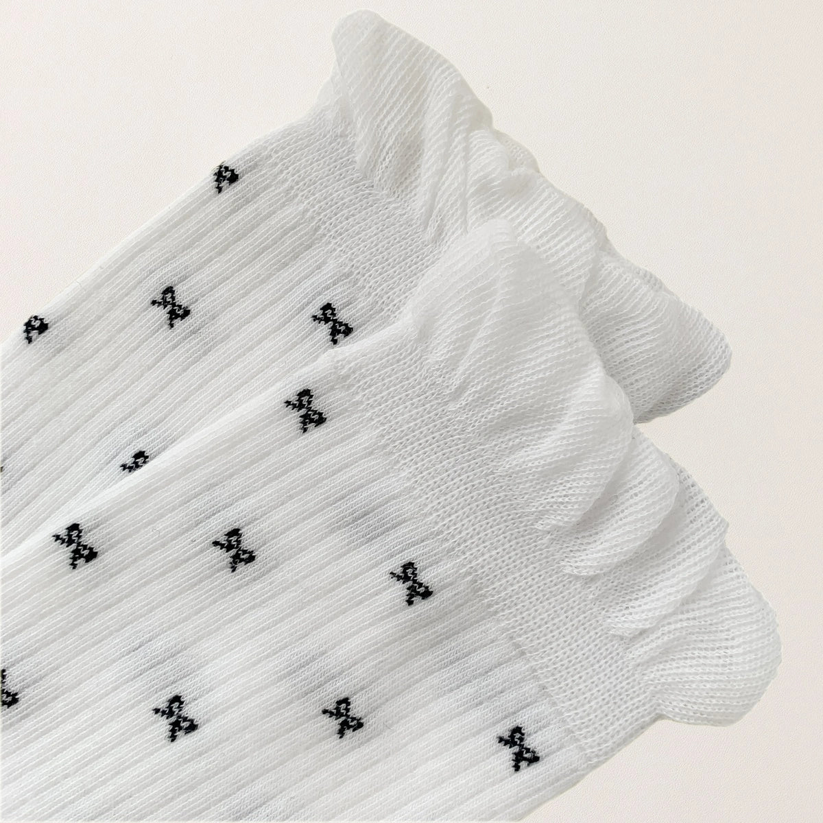 Chaussettes montantes tige côtelée. Motif petit noeud noir. Finition volant sur le haut de tige. Disponibles en blanc, gris chiné clair et noir. 