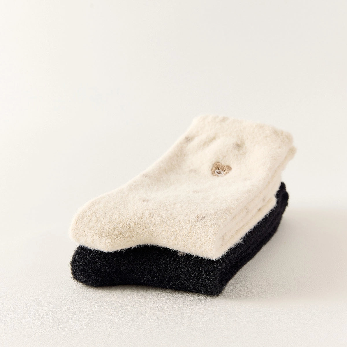 Chaussettes chaudes et douces, effet polaire, motif petits pois, tête d'ours brodée, proposée en noir et blanc cassé.