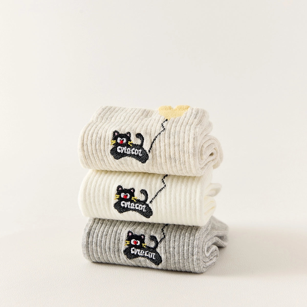 Lot de 3 chaussettes mi-hautes. Motif chat noir tenant un ballon en forme de coeur. Coloris blanc, beige et gris. Coeur contrasté.