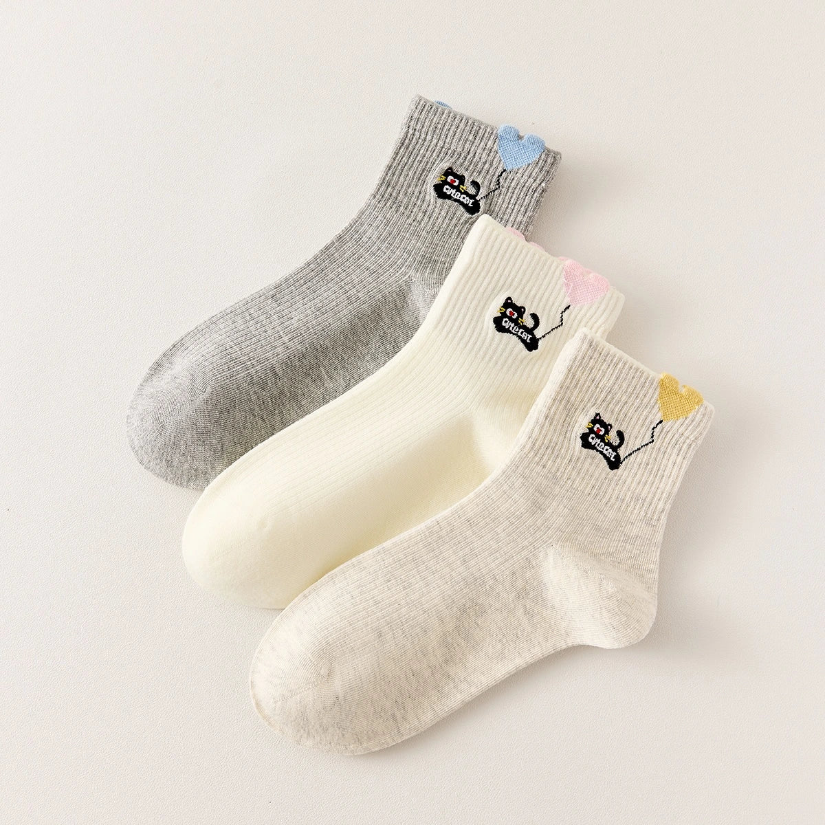 Lot de 3 chaussettes mi-hautes. Motif chat noir tenant un ballon en forme de coeur. Coloris blanc, beige et gris. Coeur contrasté.